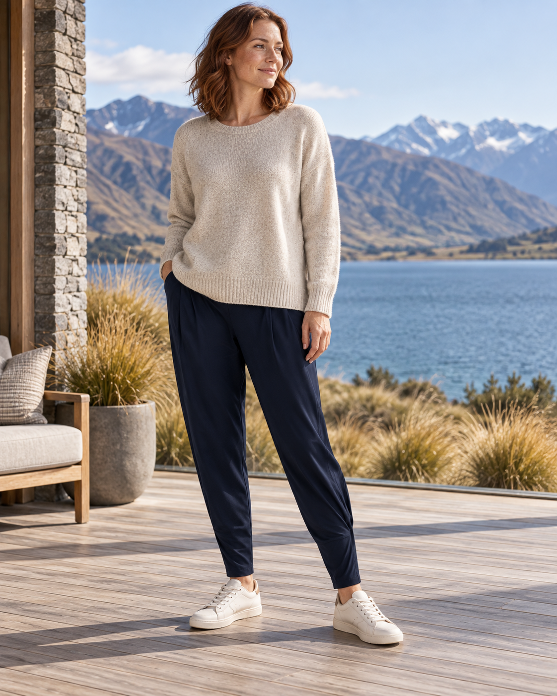 Woman wearing navy Paula Ryan Basque pants, an untucked oatmeal knit and ivory sneakers on a lakeside terrace