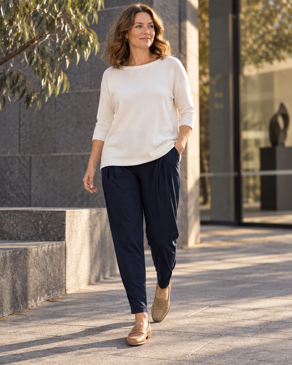 Woman wearing navy Paula Ryan Basque pants, an untucked ivory knit and tan loafers on a city street